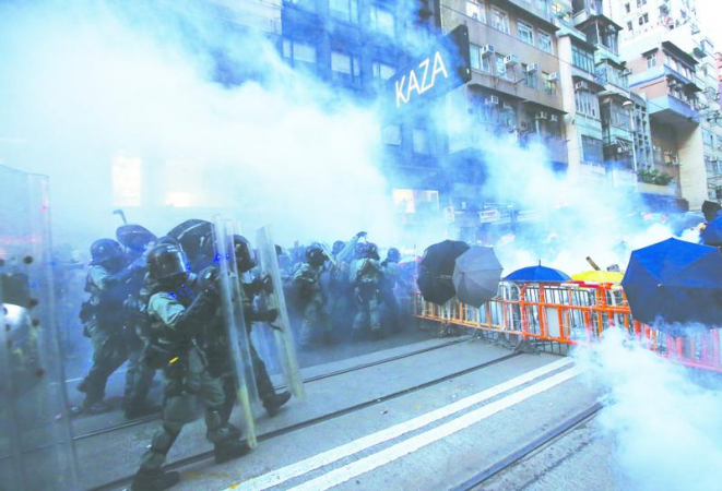 Clouds of tear gas waft down the street as police officers struggle to disperse protesters in an unauthorized rally in Sheung Wan on Sunday. (CHINA DAILY)