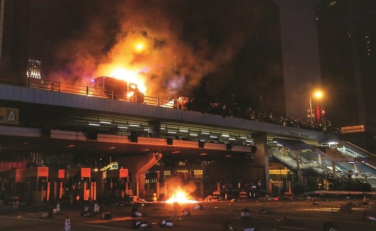 A burning police armored vehicle spews thick smoke on a flyover near Hong Kong Polytechnic University on Sunday. Radical students and rioters have turned the campus  into a stronghold in clashes with police. (PHOTO / CHINA DAILY)  