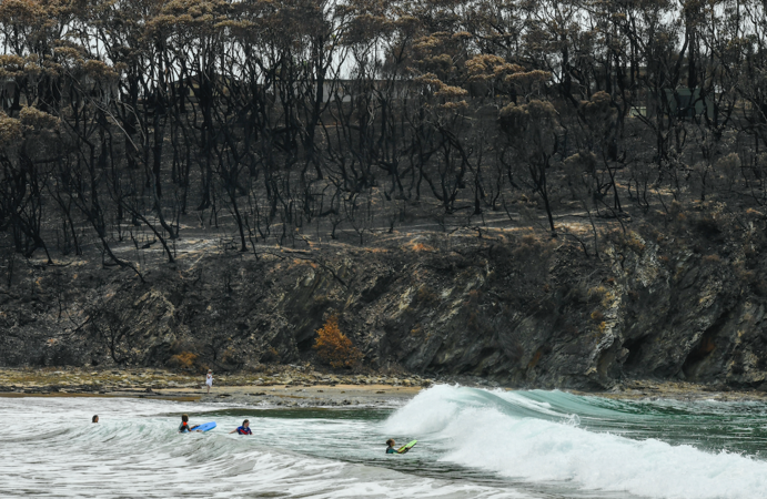 Trees burned by recent wildfires scar the backdrop last week as vacationers swim at McKenzies Beach in Malua Bay in Australia's New South Wales state. The fires torched an area larger than Portugal, killed at least 25 people and destroyed hundreds of homes. MUST CREDIT: Washington Post photo by Ricky Carioti