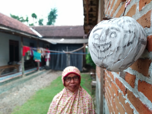 Yasmini, who lives in Wajak Kidul village in Tulungagung, East Java, looks at a 'tetek melek' mask fastened on the outer wall of her home. Some villagers have been placing the masks around their houses to 