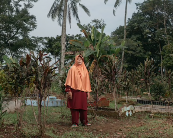 A woman named Iyum stands at Ciletuh Hilir's cemetery, where bodies of her two daughters were exhumed and reburied elsewhere. MUST CREDIT: Photo by Muhammad Fadli for The Washington Post.
