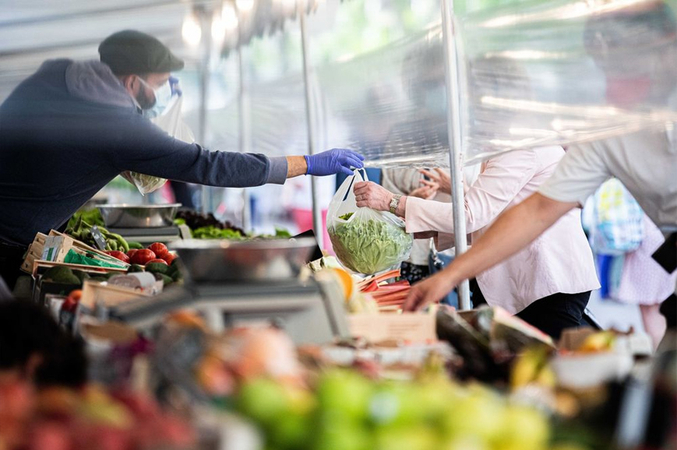 A market trader hands a customer their purchase under a protective cellophane screen on a fruit and vegetable stall in Paris on May 21. Photographer: Christophe Morin/Bloomberg