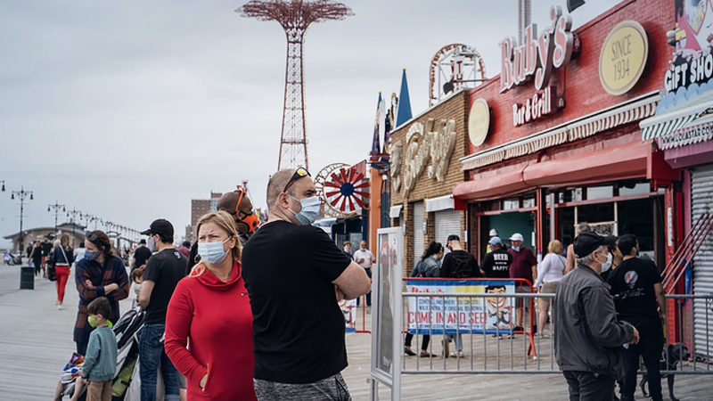 Customers wearing protective masks stand on line outside a Nathan's Famous Inc. restaurant on the Coney Island boardwalk in the Brooklyn borough of New York on May 22, 2020. MUST CREDIT: Bloomberg photo by Jeenah Moon.