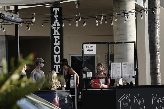 Servers wearing protective masks assist customers in the takeout area at a bar and restaurant in San Diego on June 29. (Bing Guan/Bloomberg News)
