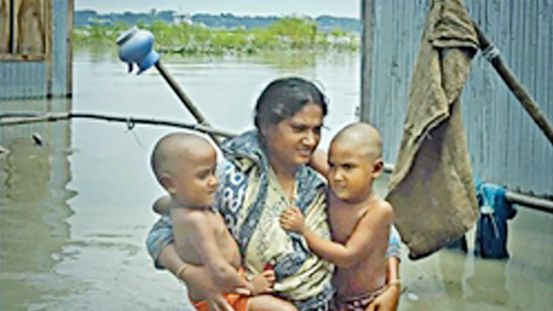 A woman trying to walk in her flooded front yard holding her two babies in Jhautia area of Munshiganj yesterday. She could save very little of her belongings from being soaked as the Padma swelled and inundated vast areas along its banks. Officials said over 5 million people across the country have been directly affected by the floods. Photo: Amran Hossain