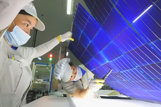 Workers make adjustments on a photovoltaic cell production line at a new energy company in Lianyungang, Jiangsu province, in August. [Photo by Geng Yuhe/For China Daily]