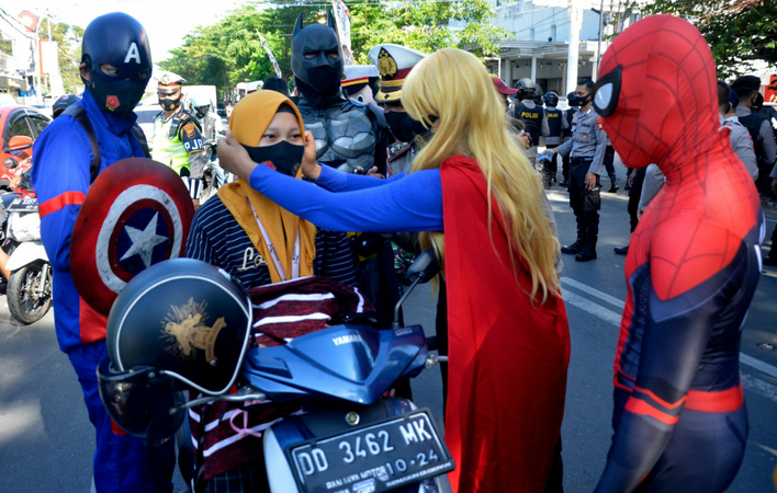 Volunteers wearing superhero costumes give away masks to road users in Makassar, South Sukawesi on Sept. 10, 2020 as part of a movement to promote mask-wearing to curb the spread of COVID-19. (Antara/Abriawan Abhe)