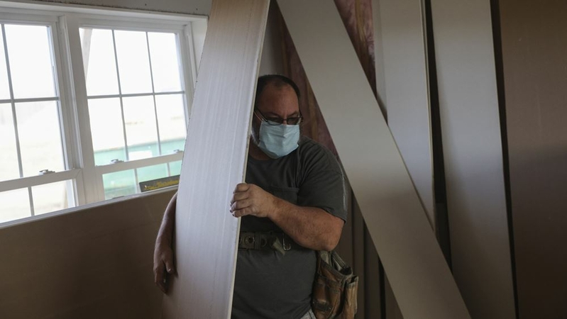 A contractor wearing a protective mask moves pieces of sheet rock while working at a home under construction at The Estates at Kelley Farms new housing development in Ballston Lake, N.Y., on Dec. 11, 2020. MUST CREDIT: Bloomberg photo by Angus Mordant.