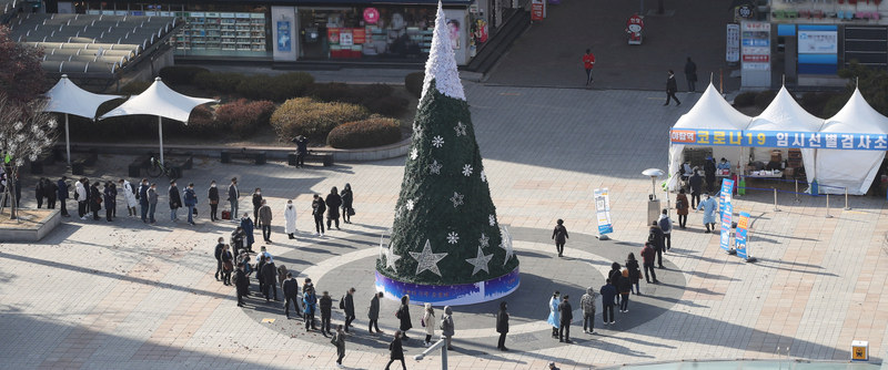 People wait in a long line around a large Christmas tree to get tested for COVID-19 at a screening center in Seongnam, just south of Seoul, on Christmas Eve on Thursday. (Yonhap)