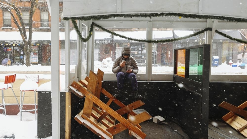 A person shelters inside a restaurant's closed outdoor dining area as snow falls in the Hells Kitchen neighborhood of New York on Dec. 17. Winter Storm Gail pounded the city as temperatures dropped to 27 degrees with frigid sustained winds up to 35 mph, making dining outdoors unbearable amid the covid-19 pandemic that has already crippled the restaurant industry. MUST CREDIT: Bloomberg photo by Angus Mordant