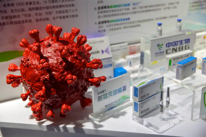 A coronavirus model is displayed next to boxes for vaccines at an exhibit by Chinese pharmaceutical firm Sinopharm in Beijing on Sept. 5. (Mark Schiefelbein/AP)