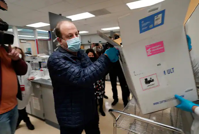 Colorado Gov. Jared Polis (D) helps put the state's first shipment of a coronavirus vaccine in a Denver freezer on Dec. 14. (David Zalubowski/AP)