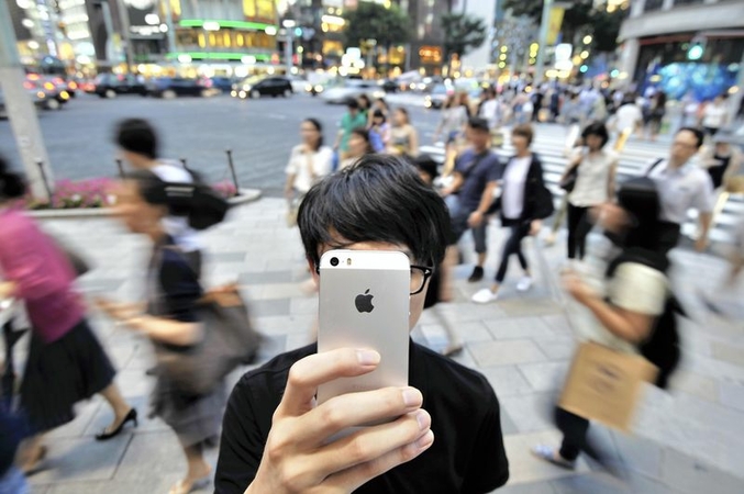 A young man holding a smartphone stands on a street in Chuo Ward, Tokyo, in July 2015. (Yomiuri Shimbun file photo)