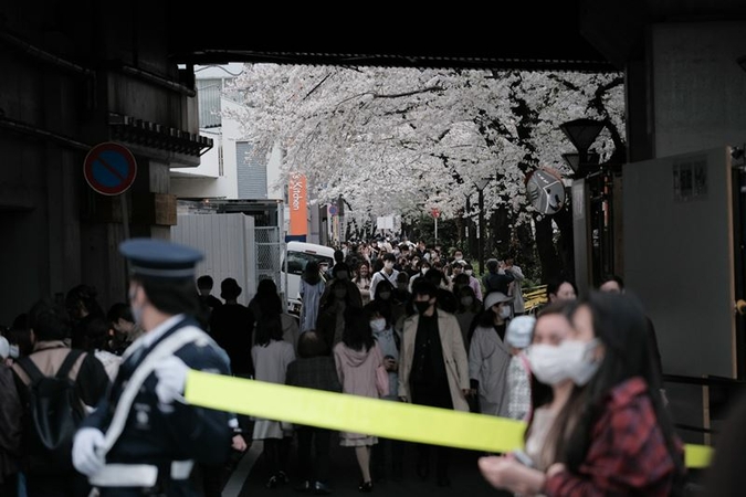 People walk past cherry blossom trees in bloom along the Meguro River in Tokyo on March 27, 2021. MUST CREDIT: Bloomberg photo by Soichiro Koriyama.