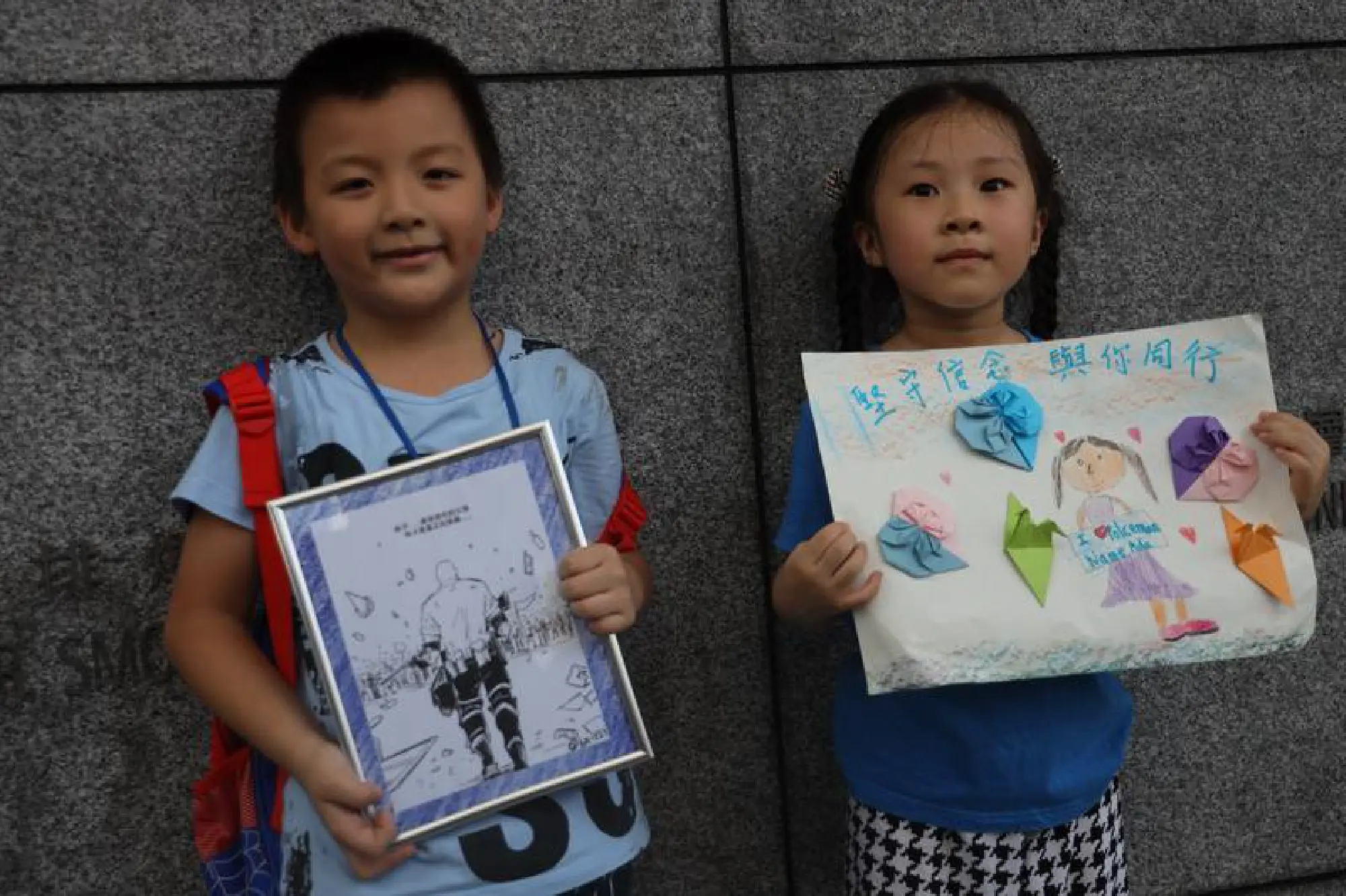 A boy and a girl pose with the illustration and a drawing to show support to Hong Kong police outside the Wan Chai police headquarters, Hong Kong, Aug 9, 2019. (PHOTO / CHINA DAILY)