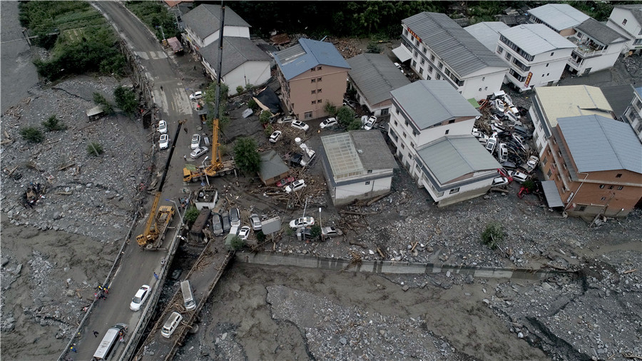 Rescuers and cranes clear damaged cars after torrential rains in Gengda township, Sichuan province, on Wednesday. LIU ZHONGJUN/FOR CHINA DAILY