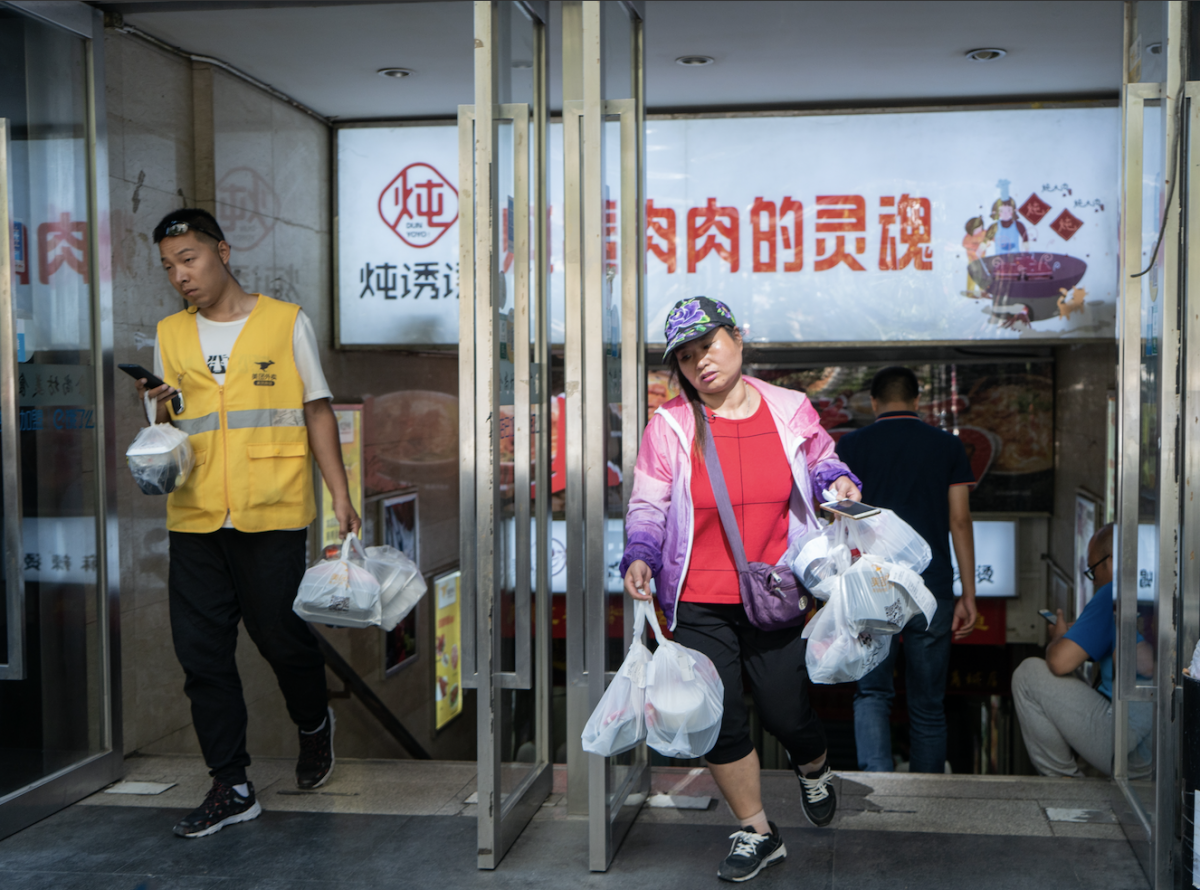 Two delivery people walk out from a food court with their hands full of packed lunch, in Beijing. MUST CREDIT: Photo for The Washington Post by Yan Cong Photo by: Yan Cong — For The Washington Post