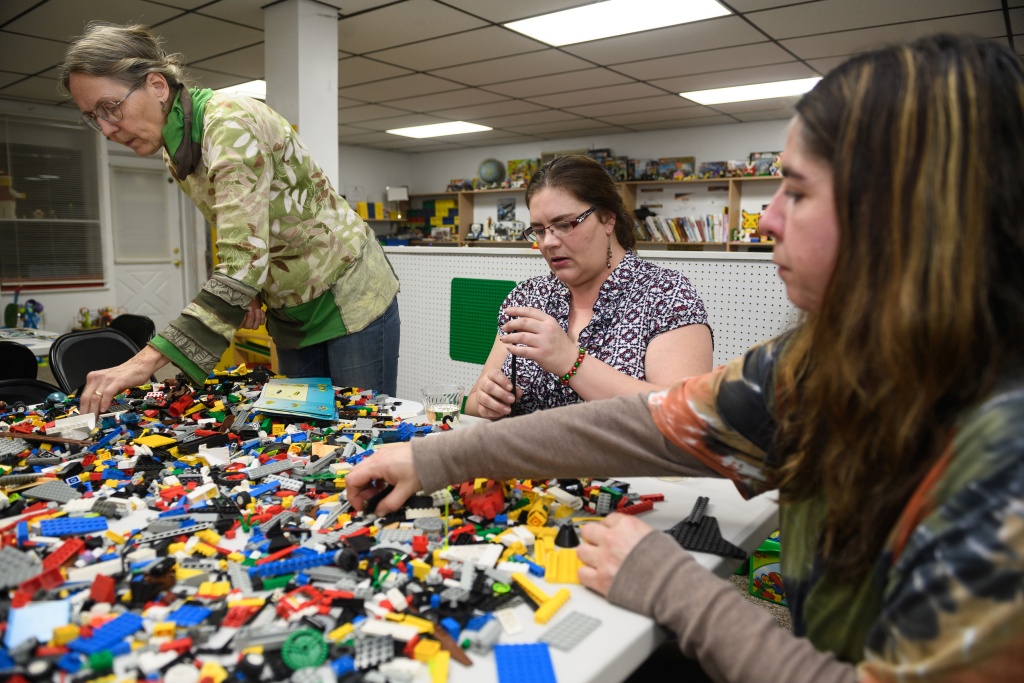 Susan Lewis, 61, left, Lori Griffith, 43, center, and CJ Paxinos, 43, all of Connellsville, Pa., build with Lego bricks during an BYOB adults-only build event at Brooke's Block Party. MUST CREDIT: Photo by Justin Merriman for The Washington Post.
