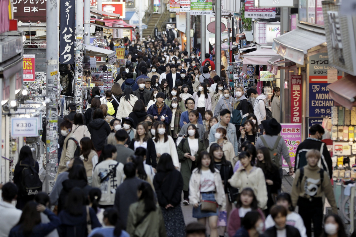 Pedestrians wearing protective masks walk past shops in Tokyo on March 26, 2020. MUST CREDIT: Bloomberg photo by Kiyoshi Ota.