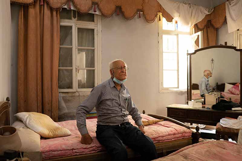 Henri Azar, 90, sits on the bed of his destroyed bedroom. MUST CREDIT: For The Washington Post by Manu Ferneini