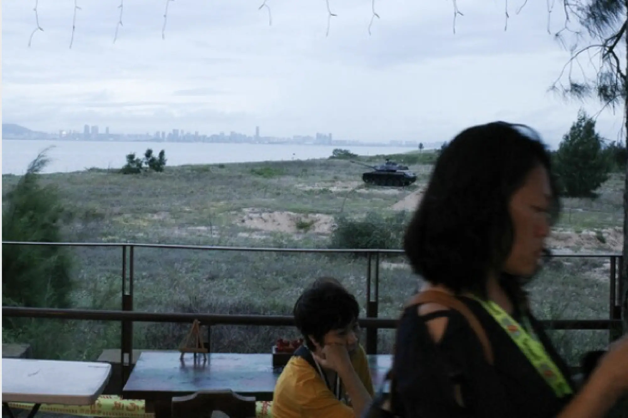 Tourists sip coffee and milk tea on Kinmen; seen in the distance is the mainland Chinese city of Xiamen, which has sent millions of tourists to the island. A tank used for the island\'s defense during the Cold War sits on the beach. MUST CREDIT: Washington Post photo by Gerry Shih.
