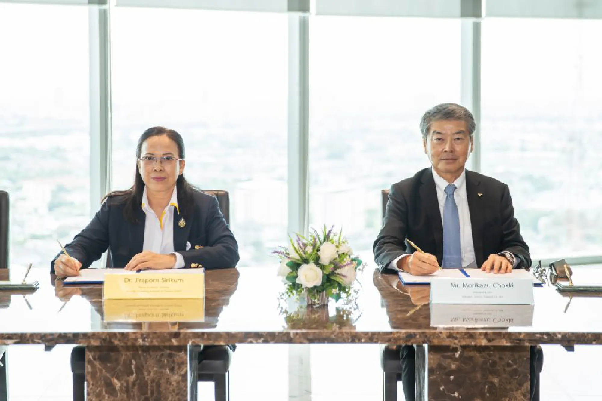 Jiraporn Sirikham, Egat's deputy governor for strategy, and Morikazu Chokki, president of Mitsubishi Motors (Thailand) Co Ltd, sign an MoU witnessed by executives from both agencies.