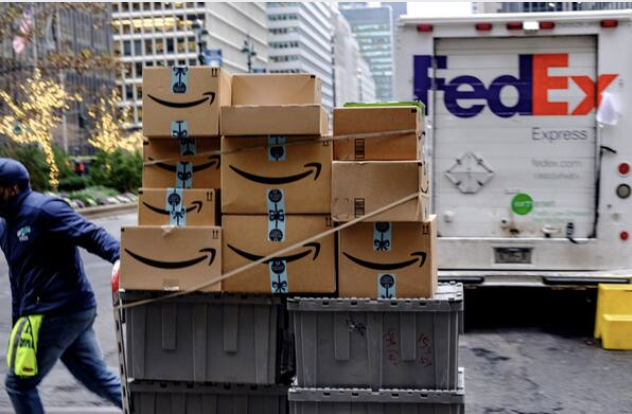 A worker pushes Amazon.com packages in front of a FedEx delivery truck in New York on Nov. 26, 2018. MUST CREDIT: Bloomberg photo by Christopher Lee
