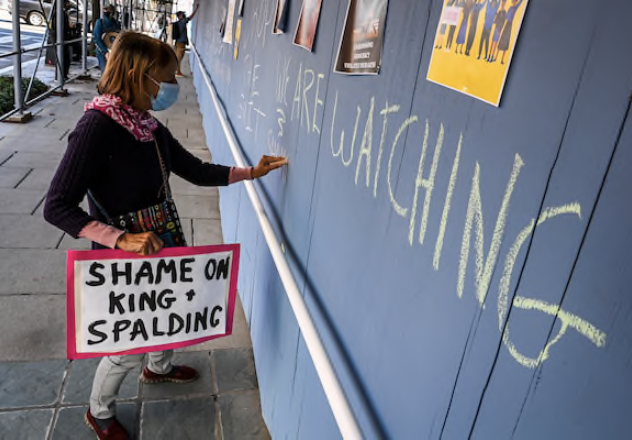 Activist Medea Benjamin writes slogans Friday on the plywood covering the front of an office building at 17th Street and Pennsylvania Avenue, home to King & Spalding law firm, protesting its involvement with Trump's election lawsuits. MUST CREDIT: Washington Post photo by Bill O'Leary