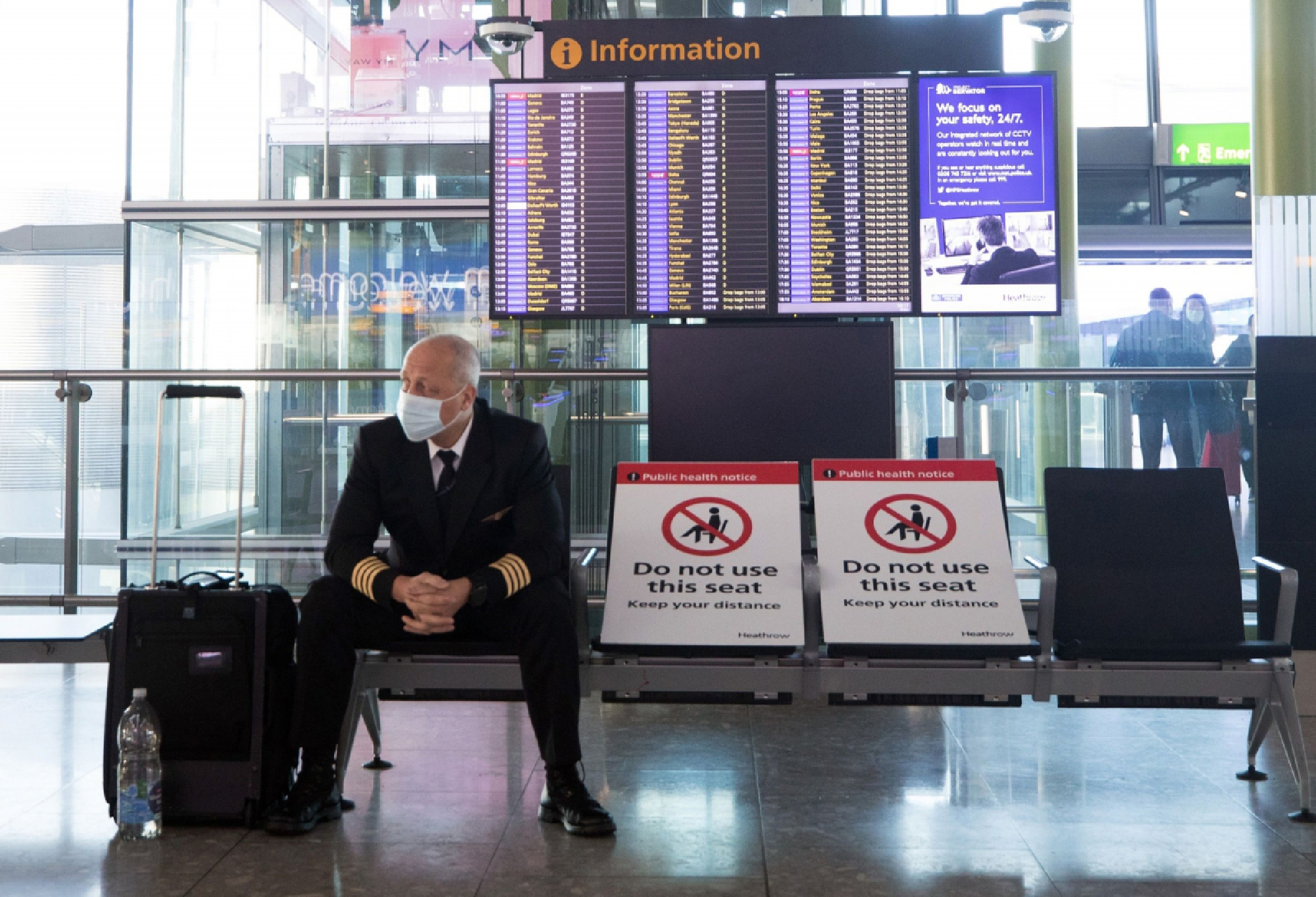 A member of flight crew sits next to social distancing signs at London's Heathrow Airport on Dec. 19, 2020. MUST CREDIT: Bloomberg photo by Chris Ratcliffe.
