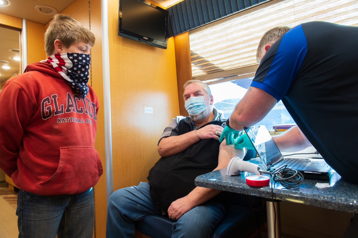 Logan, 11, and his father, U.S. Air Force veteran Mike Jellesed, 61 of Libby, Mont., after a long discussion, receives the Moderna Vaccine from RN Mark Sheldon on March 30, 2021. Photo by Tony Bynum for The Washington Post
