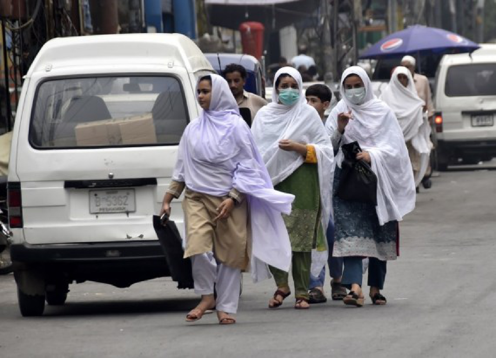 People wearing face masks walk at a market in Peshawar, northwestern Pakistan