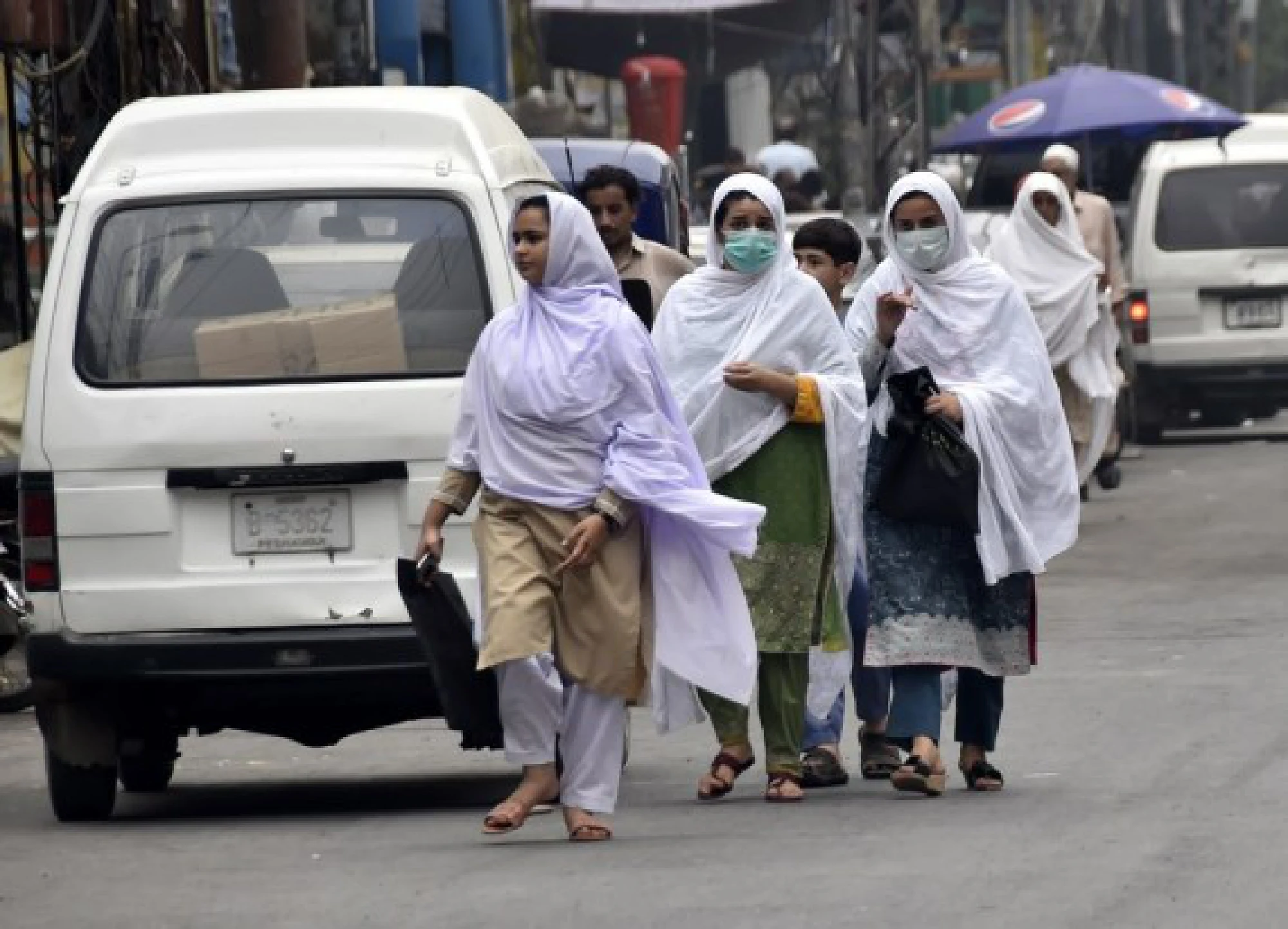 People wearing face masks walk at a market in Peshawar, northwestern Pakistan