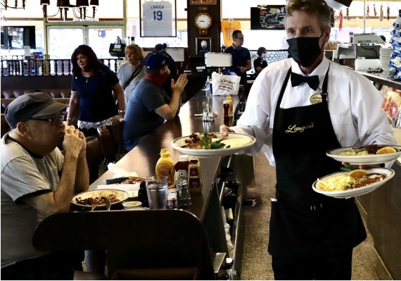 A waiter serves food at the Langer's Delicatessen-Restaurant in Westlake in Los Angeles, California, the United States, June 15, 2021.