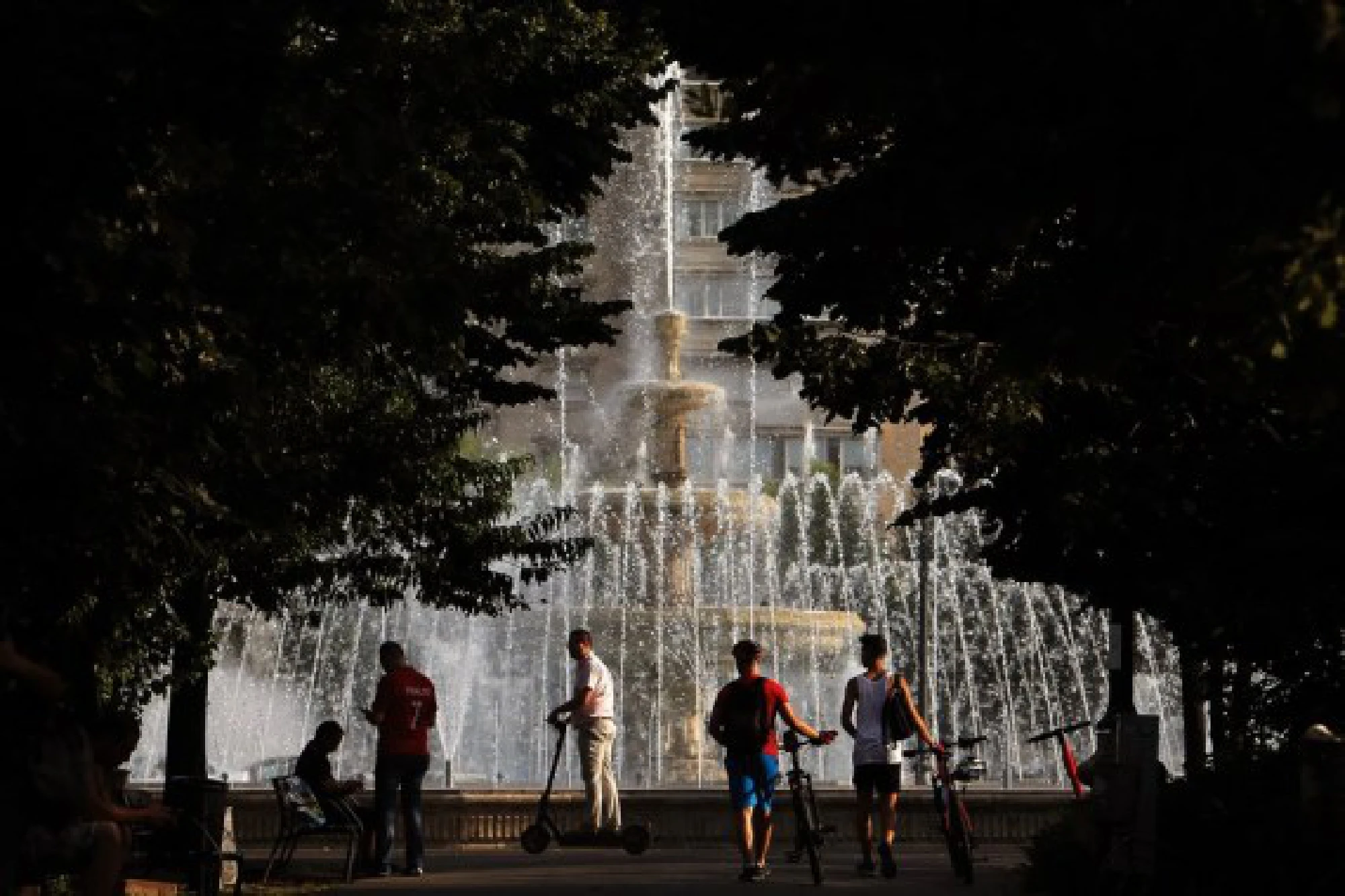 People are seen beside a fountain during a hot day in downtown Bucharest, Romania, on July 28, 2021.