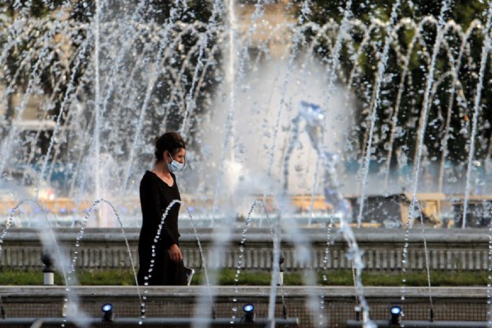 A woman walks past a fountain during a hot day in downtown Bucharest, Romania, on July 28, 2021. 