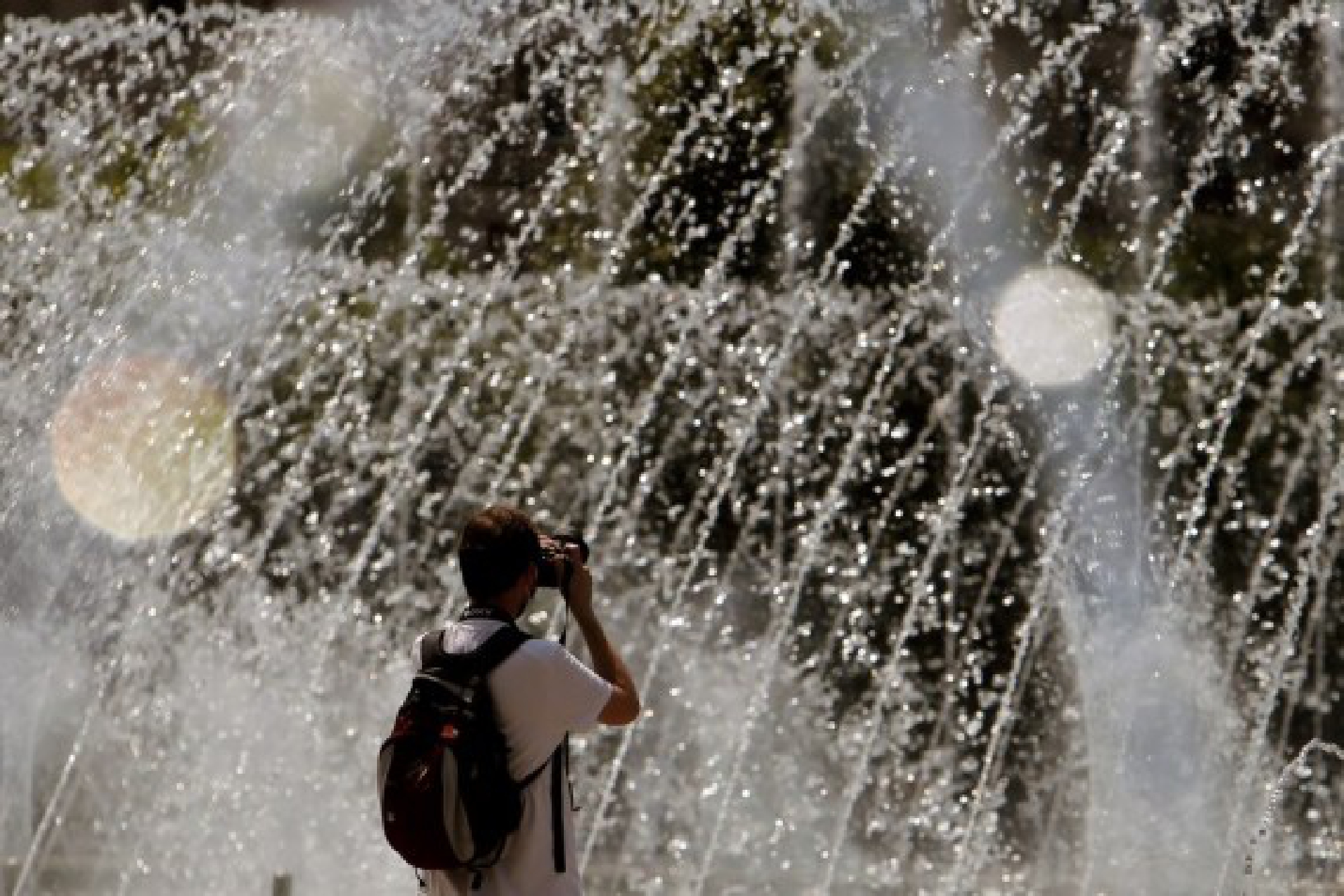 A man takes pictures of a fountain during a hot day in downtown Bucharest, Romania, on July 28, 2021.