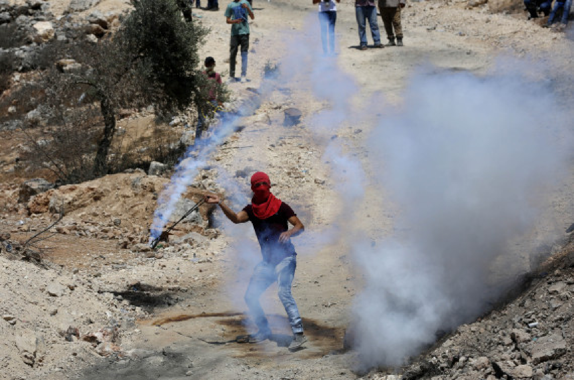A protester uses a slingshot to throw back a tear gas canister fired by Israeli soldiers in the village of Beita, south of the West Bank city of Nablus, Aug. 20, 2021. 