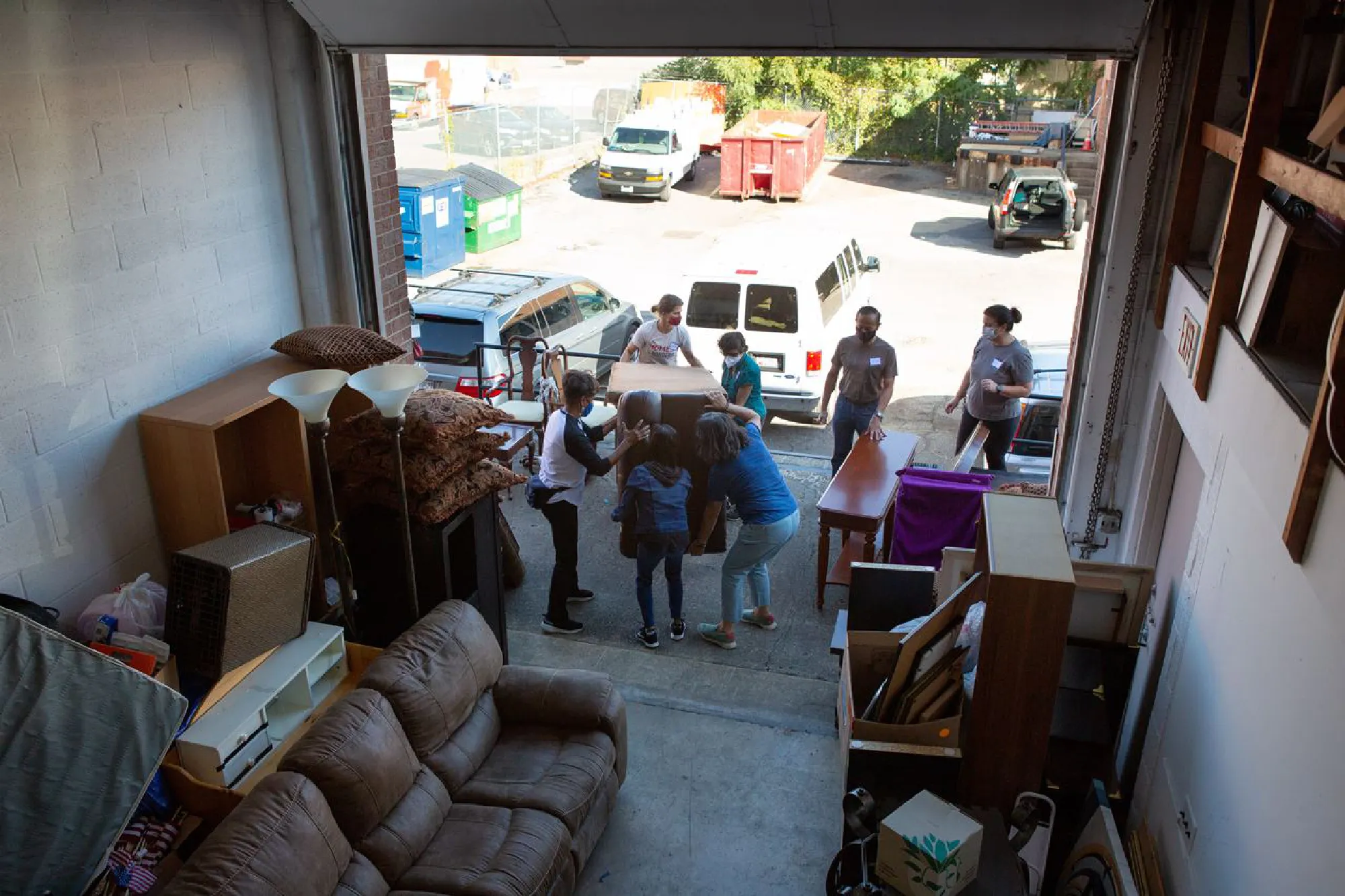 Homes Not Borders director Laura Thompson, top, red mask, works with volunteers to select and load donated furniture and household items from the organization's storage space in Landover, Md. MUST CREDIT: Photo by Allison Shelley for The Washington Post