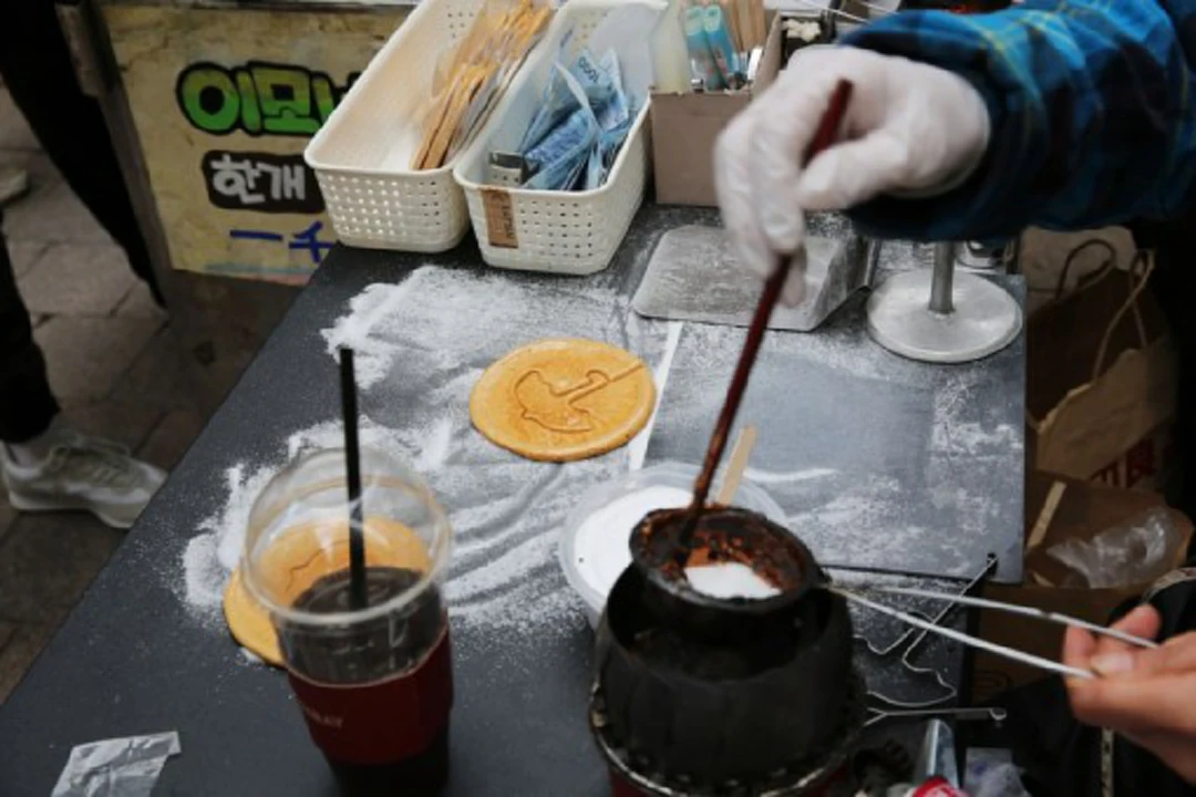 A street vendor makes a dalgona candy in Myeongdong Shopping Street in Seoul, South Korea, Nov. 13, 2021. Dalgona was a significant element of South Korean drama "Squid Game," with a deadly version of the Dalgona challenge being the second game played in the series. (Xinhua/Wang Yiliang)