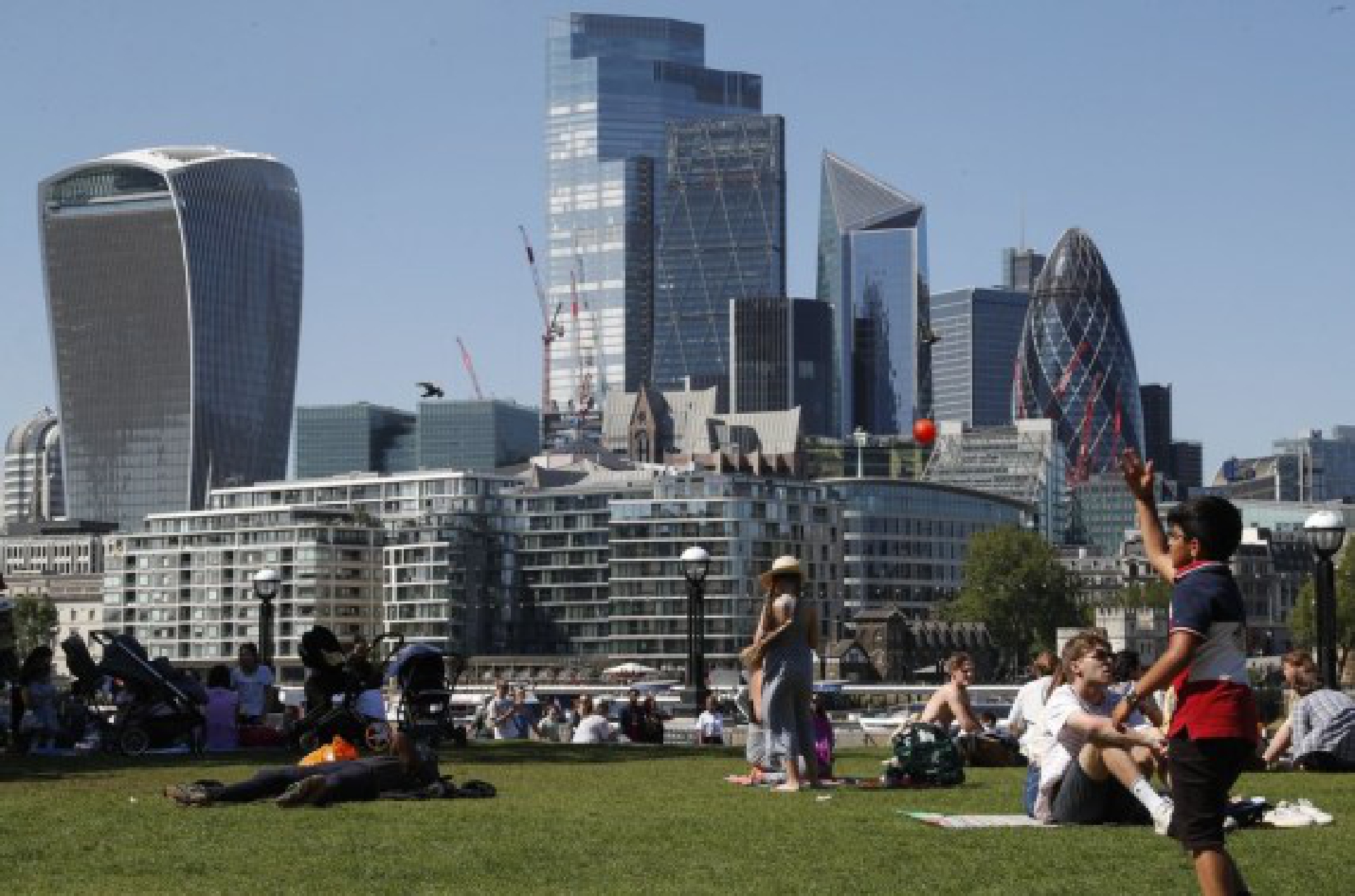People enjoy sunshine, backdropped by the City of London buildings in London, Britain, June 1, 2021. (Xinhua/Han Yan)