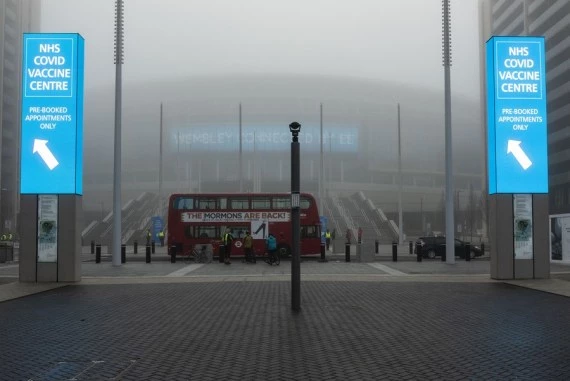 A double decker bus passes large digital signs directing the public to a mass vaccination center at Wembley Stadium in London, Britain, Dec. 19, 2021.  (Photo by Stephen Chung/Xinhua)