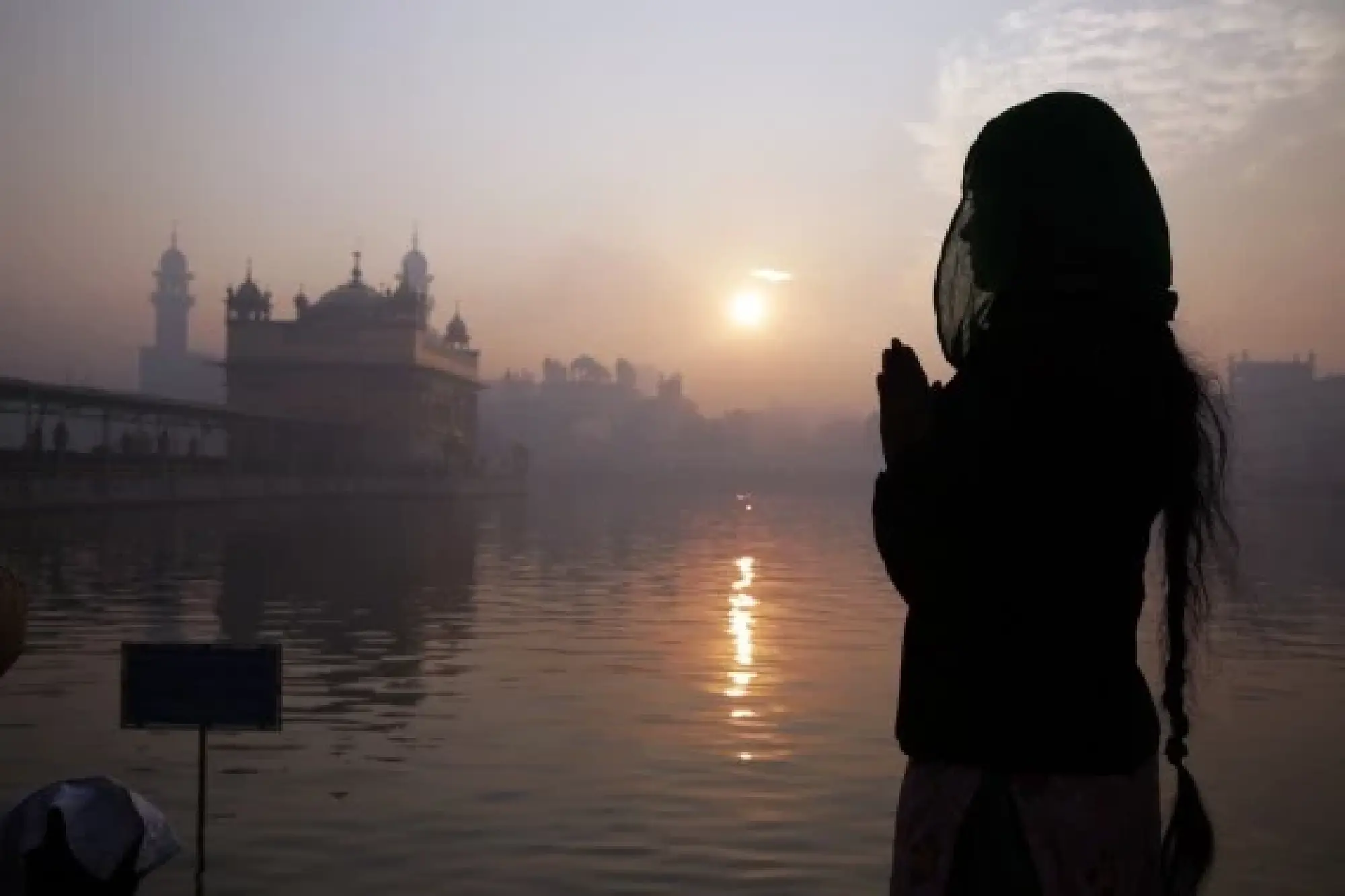 A devotee prays as the first sun of the New Year rises in the backdrop of the Golden Temple in Amritsar of India's northern state of Punjab, Jan. 1, 2022. (Str/Xinhua)
