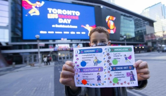 A boy wearing a face mask poses for photos with a COVID-19 vaccination "passport" after being vaccinated outside a vaccination site in Toronto, Canada, on Dec. 12, 2021. (Photo by Zou Zheng/Xinhua)
