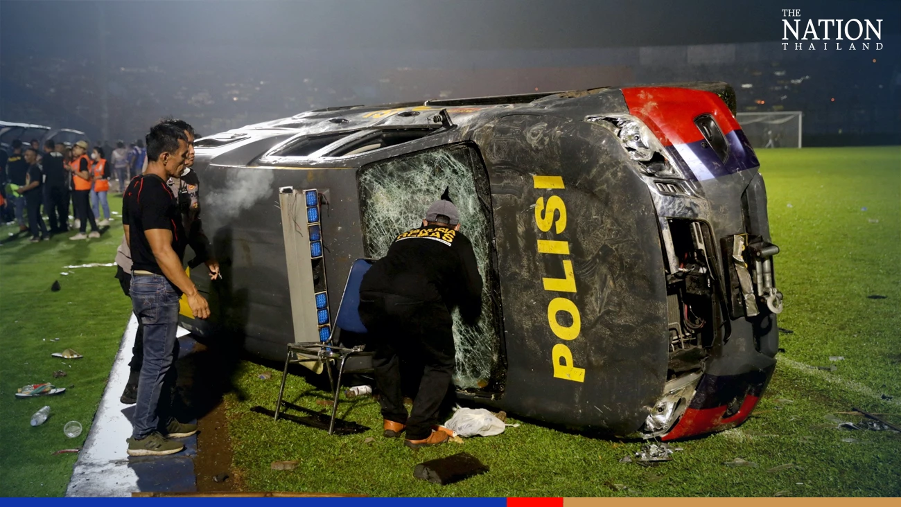 People stand next to a damaged car following a riot after the league BRI Liga 1 football match between Arema vs Persebaya at Kanjuruhan Stadium, Malang, East Java province, Indonesia, October 2, 2022, in this photo taken by Antara Foto. Antara Foto/H Prabowo/via REUTERS